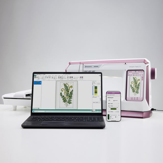 Laptop, phone, and embroidery machine on a white surface with a gray background