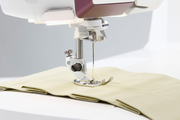 Sewing machine needle stitching fabric on a white background