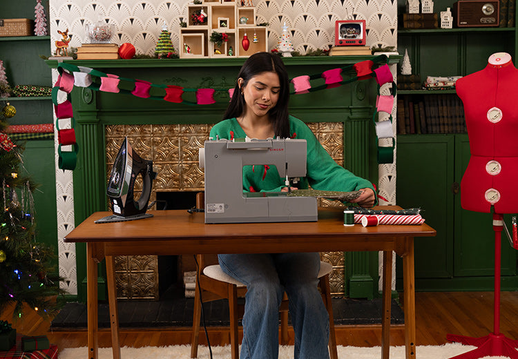 Woman using a laptop at a desk with a decorated Christmas tree and festive decorations in the background.